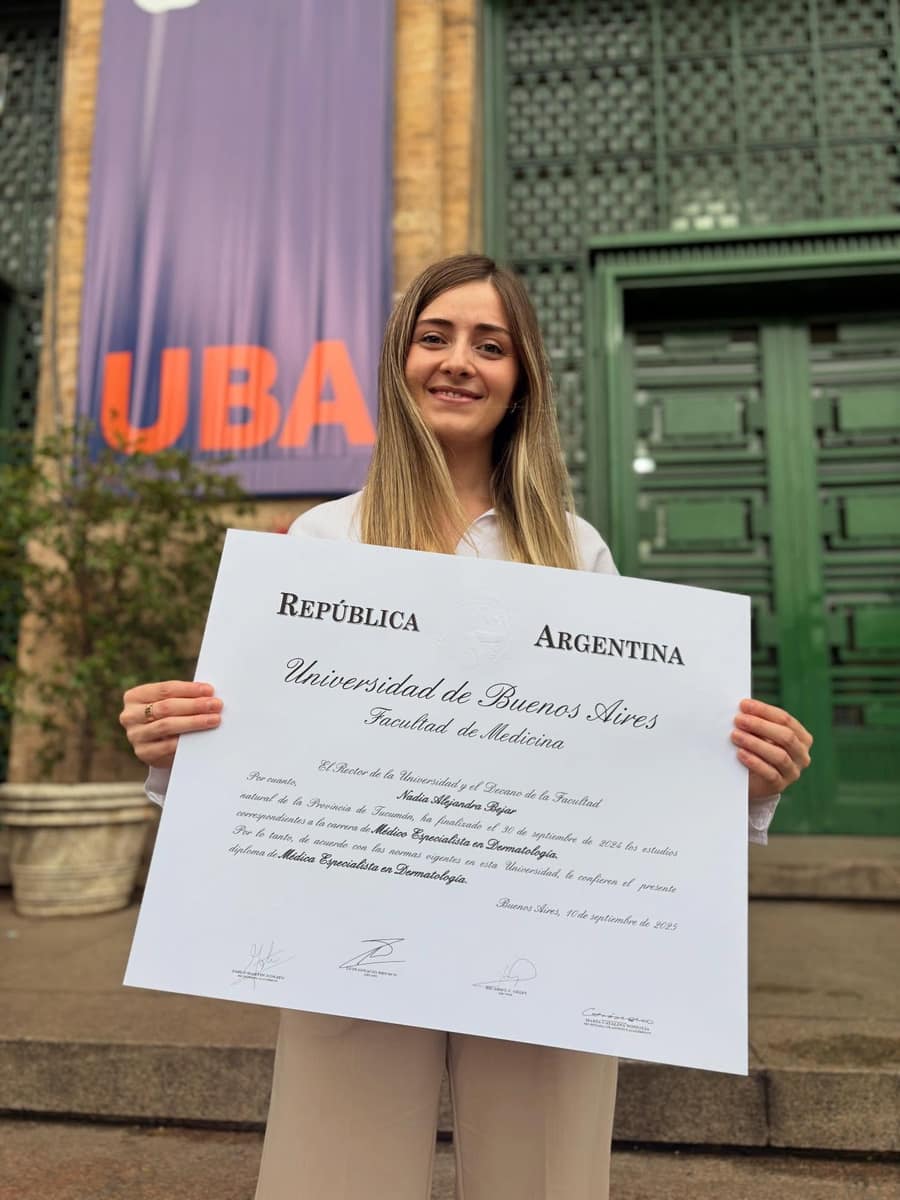 Nadia Bejar frente a la facultad con cartel de UBA y su diploma de Médica Especialista en Dermatología